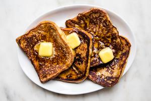 4 slices of homemade French toast topped with sliced butter and syrup on a serving platter