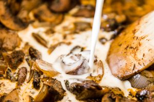 heavy cream being poured into mushroom onion mixture in a large pot to make earthy, creamy Hungarian Mushroom soup