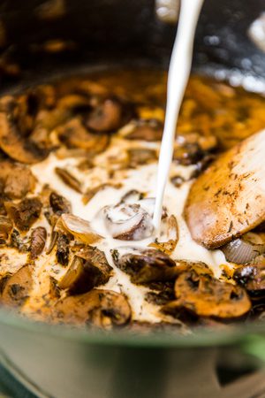 heavy cream being poured into mushroom onion mixture in a large pot to make earthy, creamy Hungarian Mushroom soup