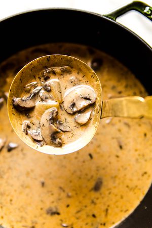 Creamy  Hungarian mushroom soup garnished with fresh parsley being ladled out of a pot for a cozy vegetarian meal.