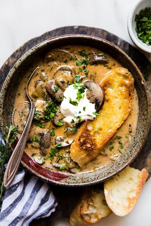 A bowl of creamy Hungarian mushroom soup topped with sour cream, fresh parsley & pepper served with crusty bread