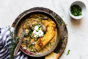 A bowl of creamy Hungarian mushroom soup topped with sour cream, fresh parsley & pepper served with crusty bread