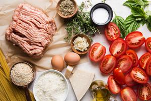 ingredients laid out for italian chicken meatballs, tomatoes, parmesan cheese, breadcrumbs, egg and garlic