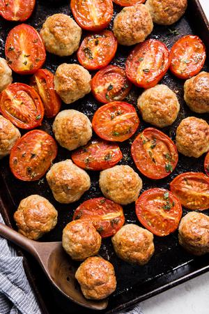 Italian chicken meatball and roasted tomatoes on a baking sheet with a serving spoon