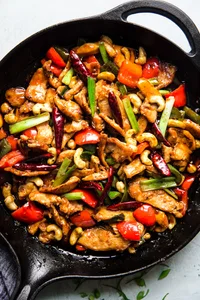 kung pao chicken in a cast iron skillet made with bell peppers, green onions, cashews, ginger, garlic and dried chili peppers