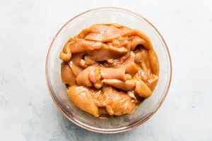 thinly sliced raw chicken breast in a glass bowl marinading in soy sauce and cornstarch to make homemade kung pao chicken