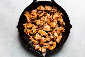 thinly sliced chicken marinaded in soy sauce and corn starch being cooked in a skillet with sesame oil for kung pao chicken