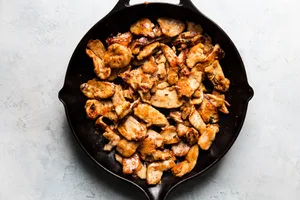 thinly sliced chicken marinaded in soy sauce and corn starch being cooked in a skillet with sesame oil for kung pao chicken
