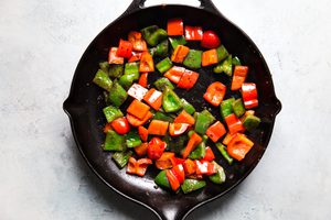 diced red and green bell peppers being cooked in sesame oil in a skillet in this easy kung pao chicken recipe