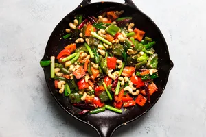 chicken and kung pao sauce added to a pan with bell peppers, green onions, cashews, ginger, garlic and dried chili peppers