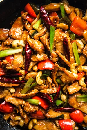 kung pao chicken in a cast iron skillet made with bell peppers, green onions, cashews, ginger, garlic and dried chili peppers