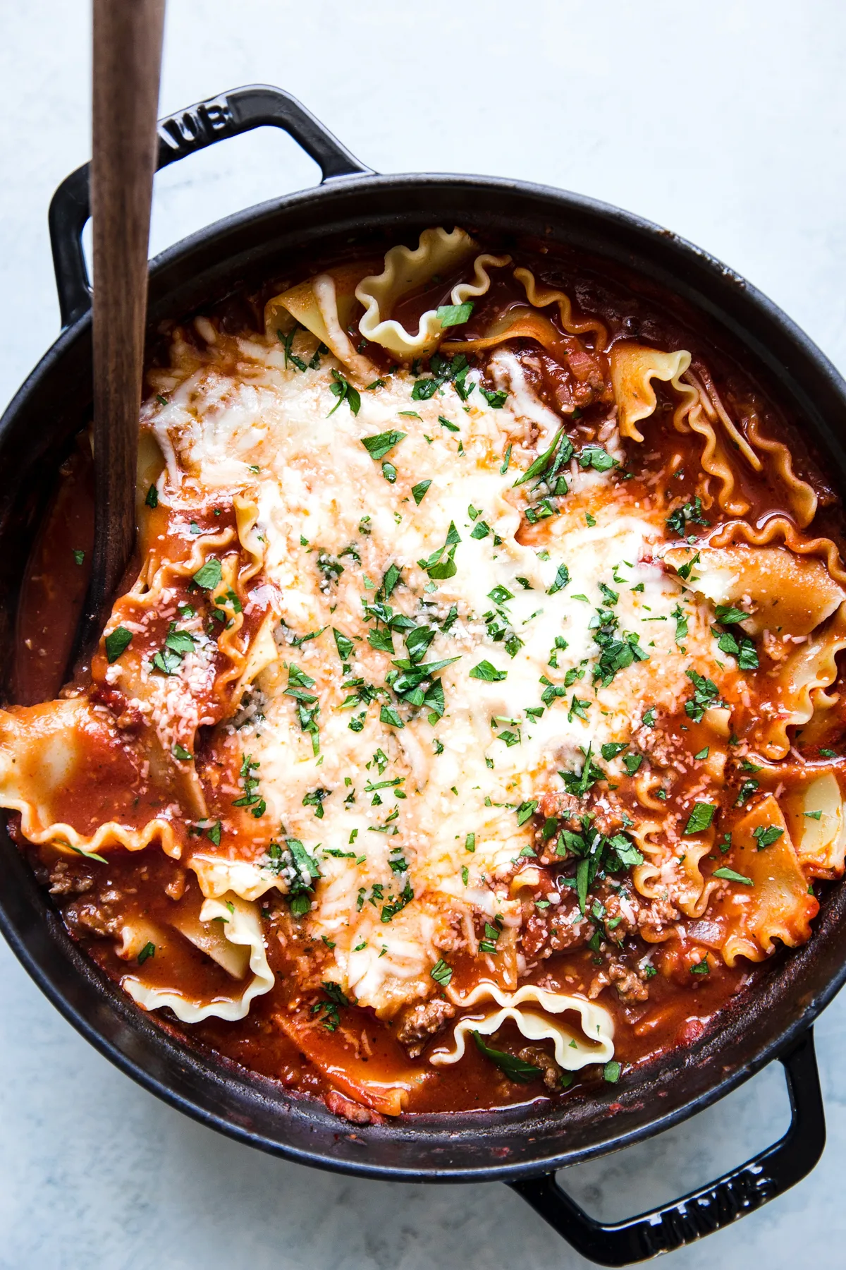 A large soup pot filled with cheesy lasagna soup being stirred with a wooden spoon