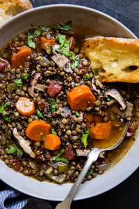 lentil stew with quinoa and mushrooms in a ceramic bowl with crusty buttered bread.