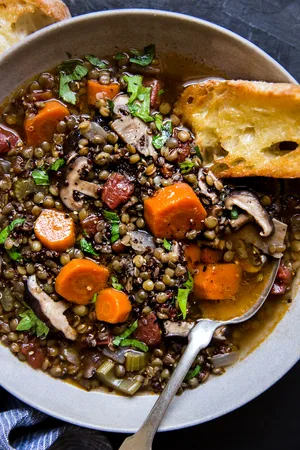 lentil stew with quinoa and mushrooms in a ceramic bowl with crusty buttered bread.