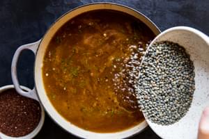 large soup pot with vegetable broth, cooked vegetables with french lentils being poured into the pot.