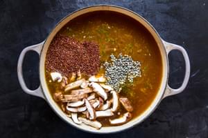 large soup pot with vegetable broth, uncooked quinoa, uncooked french lentils and sliced mushrooms.