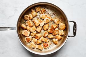 bite sized chicken breast pieces seasoned with salt being browned in olive oil in a skillet