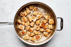 bite sized chicken breast pieces seasoned with salt being browned in olive oil in a skillet