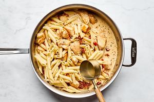 cooked pasta noodles being stirred in a skillet with chicken and creamy sun-dried tomato and Parmesan sauce