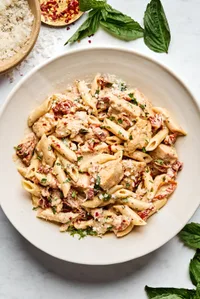 a bowl of marry me chicken pasta made with garlic, cream, Parm, sun dried tomatoes, italian seasoning topped with fresh basil