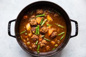 homemade meatball stew with green beans, celery, carrots, onion, potatoes and ground beef in a pot on the counter