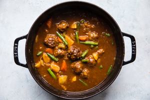 homemade meatball stew with green beans, celery, carrots, onion, potatoes and ground beef in a pot on the counter