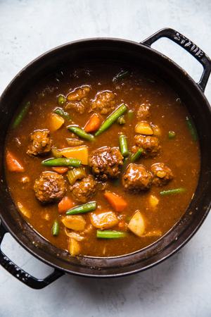 homemade meatball stew with green beans, celery, carrots, onion, potatoes and ground beef in a pot on the counter
