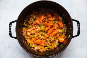cooked onion, celery, carrots and garlic being stirred with tomato paste and thyme in a pot