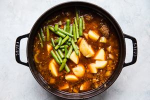 cooked vegetables, tomato paste, thyme, beef stock, beef bouillon, meatballs, potatoes and green beans in a pot