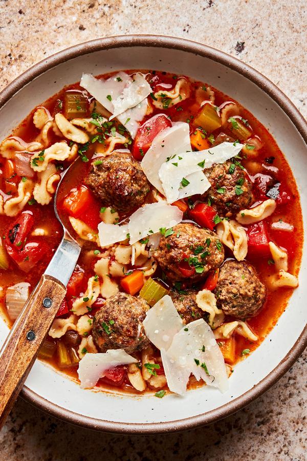 homemade meatball soup in a bowl with a spoon topped with fresh shaved parmesan cheese and fresh parsley