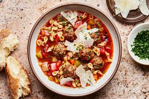 a bowl of meatball soup topped with parmesan and parsley surrounded by crusty bread and bowls of extra parmesan and parsley