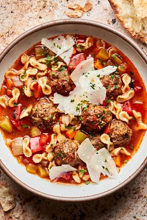 a bowl of homemade meatball soup topped with fresh shaved parmesan cheese and fresh parsley