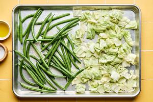 green beans and cabbage being tossed with olive oil and salt on a sheet pan