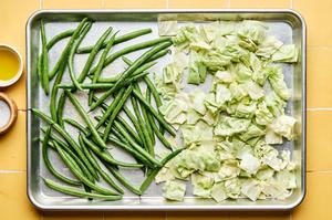 green beans and cabbage being tossed with olive oil and salt on a sheet pan