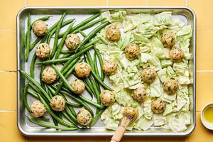 chicken meatballs, green beans and cabbage being brushed with olive oil on a sheet pan