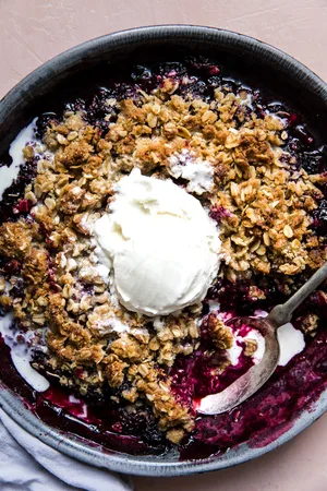 mixed berry crisp with an oat crumble topping in a baking dish topped with a scoop of vanilla ice cream