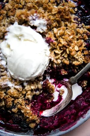 mixed berry crisp with an oat crumble topping in a baking dish topped with a scoop of vanilla ice cream