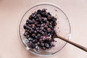 mixed berries being stirred in a bowl with sugar, salt, flour, lemon juice and cinnamon