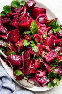 Moroccan beet salad with red onions and fresh herbs on a white platter with a spoon