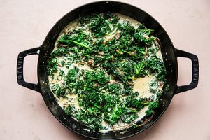 shallots, garlic, kale heavy cream, Parmesan, mustard, thyme, nutmeg and salt being cooked in a skillet