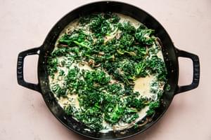 shallots, garlic, kale heavy cream, Parmesan, mustard, thyme, nutmeg and salt being cooked in a skillet