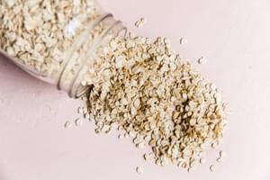 Uncooked oats spilling out of a jar onto a light pink surface