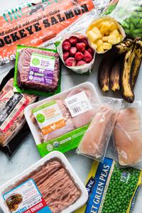 frozen chicken thighs, frozen ground beef, frozen fruit and frozen vegetables spread out on a blue surface