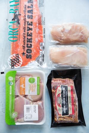 frozen salmon, frozen chicken breasts, frozen chicken thighs, frozen bacon on a blue surface