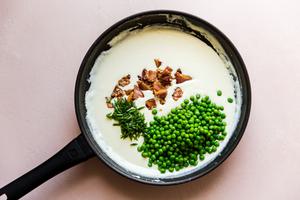 adding peas, pancetta and chives to cream pasta sauce in a pan
