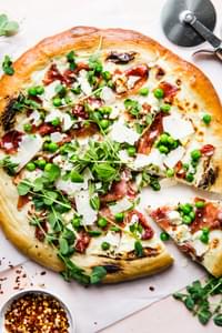 Pea and prosciutto pizza with goat cheese cream sauce parmesan cheese spring pizza with one slice taken out.