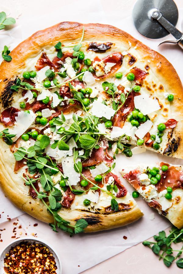 Pea and prosciutto pizza with goat cheese cream sauce parmesan cheese spring pizza with one slice taken out.