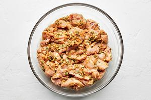 chicken thighs cut up in 1 inch pieces being marinated in peanut sauce in a glass bowl