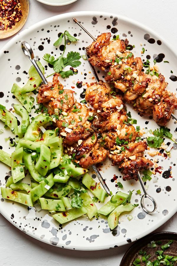 Peanut Sauce Marinated Chicken Skewers sprinkled with crushed peanuts on a plate served with cucumber salad
