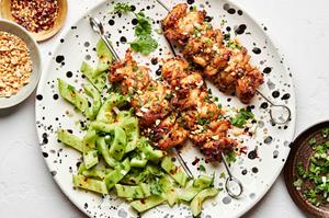 Peanut Sauce Marinated Chicken Skewers sprinkled with crushed peanuts on a plate served with cucumber salad